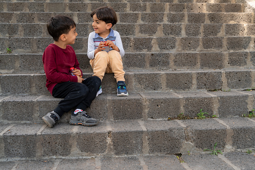 brothers sitting on stone stair steps. \nThey spend time together. they have a water bottle in their hand. Shot with a full-frame camera in daylight.