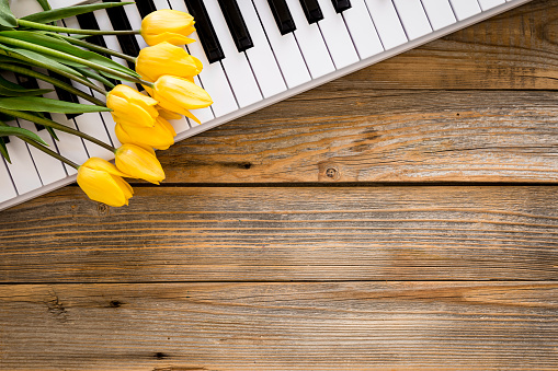 Keys of a white piano and a bouquet of yellow tulip flowers on a wooden background, top view, copy space.