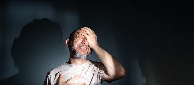 Sad man suffering from headache or migraine. Stressed guy with painful facial expression feeling terrible weakness or depression. Isolated on dark background.