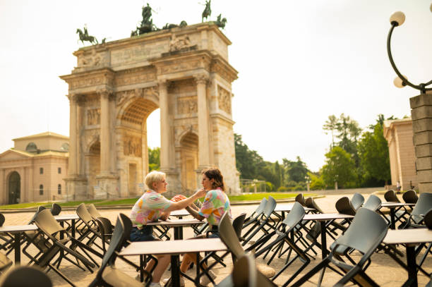Lovely couple holding hands at cafe. Arco della Pace, Milano, Italy at the background