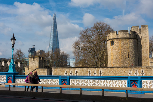 Pedestrians walking across London Bridge with the Tower of London and the Shard in the background