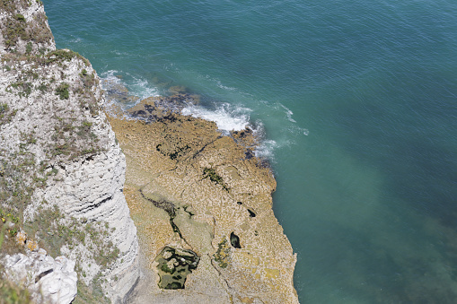 Beautiful view of the rocky coastline and the waves of the north sea breaking against it on a clear sunny summer day in tretat, Normandy, close-up view from above.