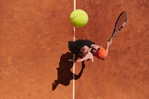 Top view of a professional tennis player serves the tennis ball on the court with precision and power.