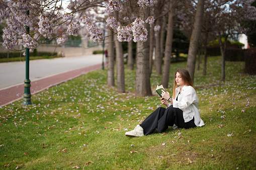 Young woman reading a book under the blossoming tree in spring. spring concept