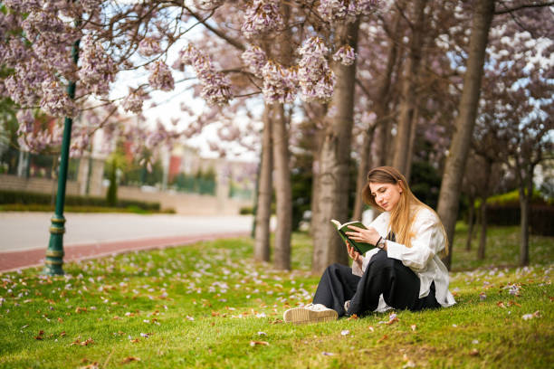 istock Young woman reading a book under the blossoming tree in spring. spring concept 1492440567