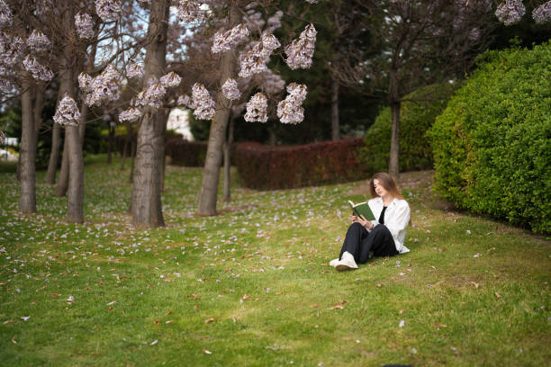 istock Young woman reading a book under the blossoming tree in spring. spring concept 1492440598