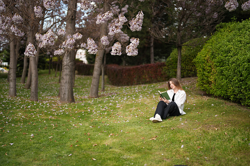 Young woman reading a book under the blossoming tree in spring. spring concept