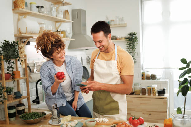Smiling young couple using phone while making pizza in a domestic kitchen