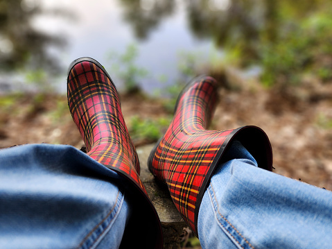 Woman sitting by pond wearing plaid rubber boots.