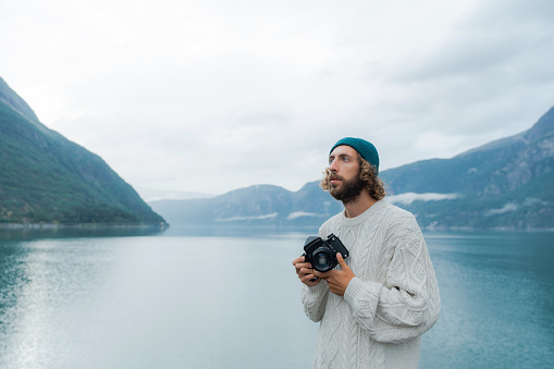 Man  in white sweater photographing Norwegian scenic landscape with film camera