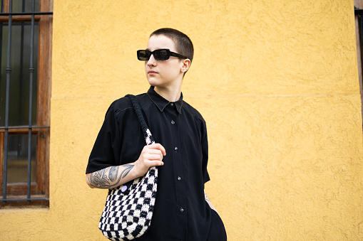 Portrait of a transgender male in the cool black outfit. He is looking away. Yellow background