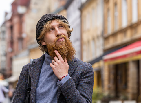 Portrait of young man tourist walking in urban city street background in summer daytime. Redhead bearded guy traveler smiling having positive good mood enjoying outdoors. Town lifestyles, vacation