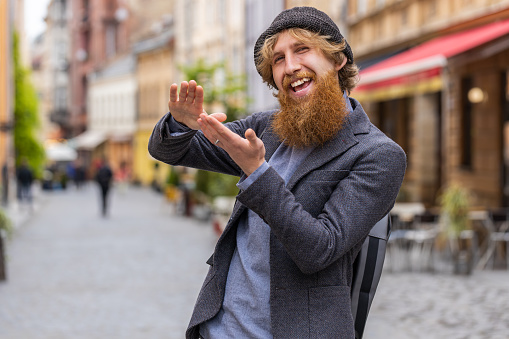 Cheerful rich young bearded man showing wasting throwing money around hand gesture, more tips earnings, big profit, win lottery, share, celebrate. Redhead guy walking in urban city street outdoors