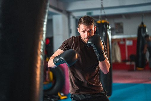 Handsome young Caucasian male kickboxer punching a boxing bag at the gym. He is focused and determined. He is strong and fit.