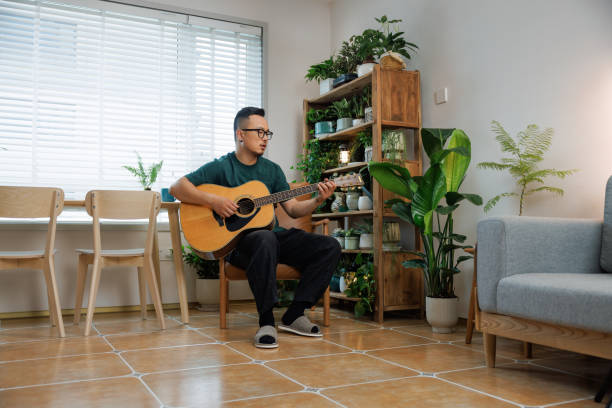 asian middle aged man playing guitar at home