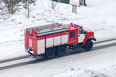 A red fire truck or Fire engine drives down a snowy street in winter