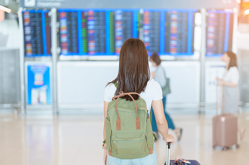 Young woman with bag and luggage looking to flight time information board in international airport, before check in. Travel, Vacation, trip and Transport concept