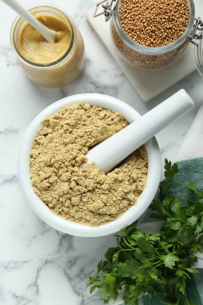istock Mortar with aromatic mustard powder, grains and parsley on white marble table, flat lay 1492483269