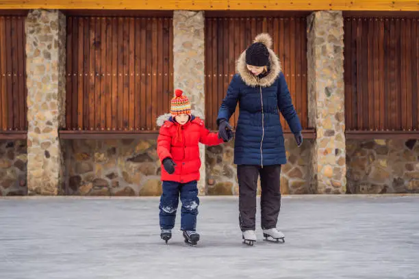 young mother teaching her little son ice skating at outdoor skating rink. Family enjoy winter on ice-rink outdoors.