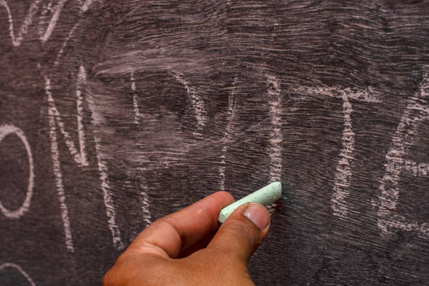 istock Male left hand writing on black board holding chalk. Teaching concept. 1492493876