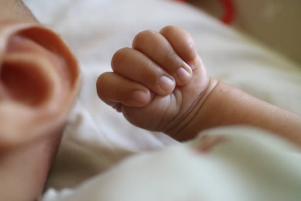 The newborn baby is holding their father's hand