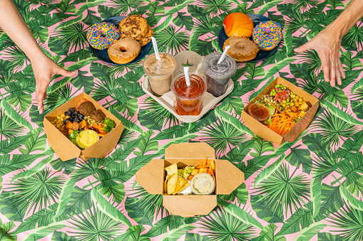 30 degree/Overhead shot of hands reaching for vegan food varieties, desserts and smoothies on a picnic blanket.