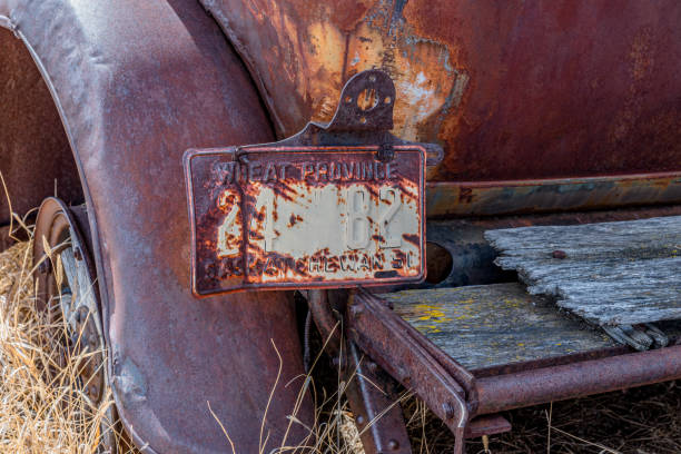 An old, rusty Saskatchewan license plate attached to an abandoned classic car