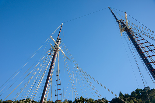 Warkworth New Zealand - March 8 2011;Two masts with rigging rising skyward above old fashioned sailing boats moored alongside waterfront pier on Mahurangi River