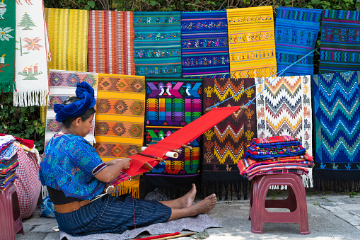 Santa Catarina Palopó, Solalá, Guatemala - October 06 2019: Mayan woman is selling and weaving tablecloths with her backstrap loom on a street in Santa Catarina Polopó.