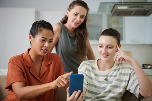 Smiling young woman showing new application on smartphone to friends