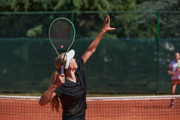 giovani ragazze in una vivace partita di tennis in una giornata di sole, dimostrando le loro abilità ed entusiasmo su un moderno campo da tennis. - skill vitality agility strength foto e immagini stock