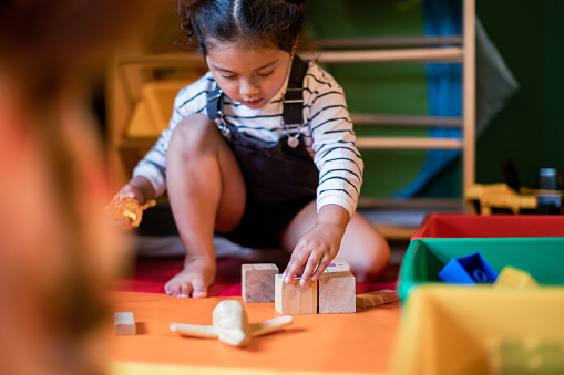 A cute girl with autism spectrum disorder playing and organizing toys by shapes and colors and size. She is 3 and a half years old and focuses her attention on categorizing wooden toys by shapes, colors, and size.