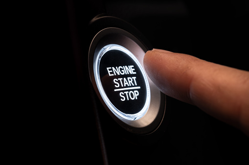 The driver's hand is pressing the car start button. Concept of transportation and technology