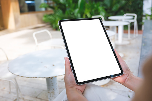 Mockup image of a woman holding digital tablet with blank white desktop screen in the outdoors cafe
