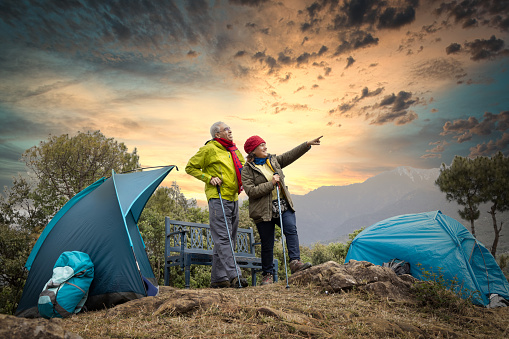 senior couple standing beside their tent on hill.