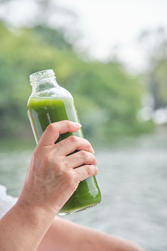 Unrecognizable person drinking green juice from a glass bottle. Concepts: wellness, nourishment, healthy and sustainable lifestyle.