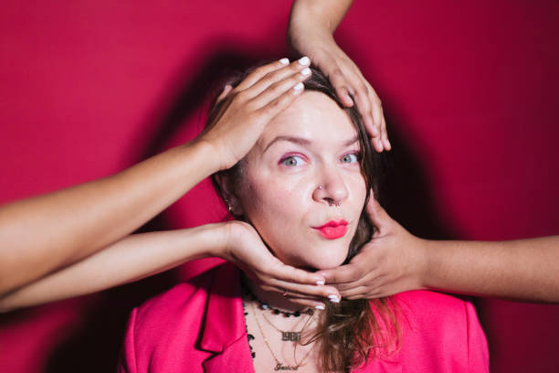 Studio portrait of a woman with hands all over her head and making a silly face to the camera in front of a pink backdrop