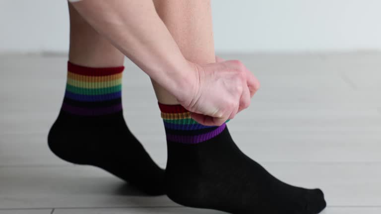 Man putting on black socks with rainbow multicolored stripes