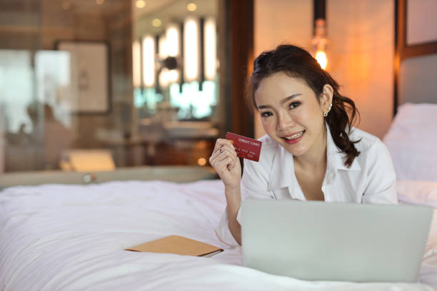 istock Happy asian woman in casual lying on bed and holding credit card while using computer in hotel for online shopping payment, beauty businesswoman with bedroom background. Lifestyle technology concept 1492529035