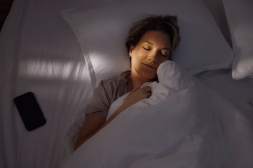 Above view of young smiling woman sleeping in bed at night.