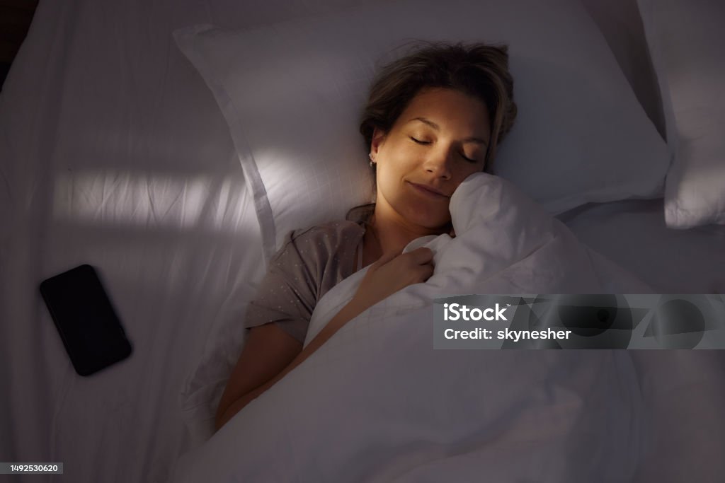 Serene woman sleeping in bed at night. Above view of young smiling woman sleeping in bed at night. Sleeping Stock Photo