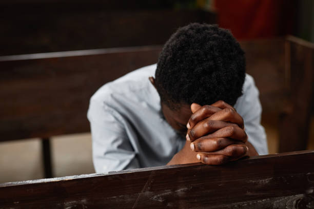 Man praying in a pew, stain glass in the background.