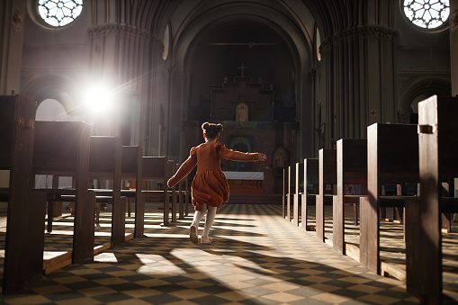 Rear view of little girl running between the benches in baptist church with old architecture