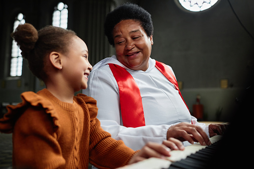African American mature woman teaching little girl to play piano during performance in church