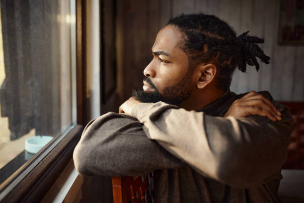 istock Serious black man looking through window from home. 1492533961