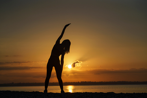 Young woman exercising on the beach at sunrise