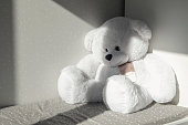White big soft bear toy sitting on the child bed in the room. Sunlight falls on it