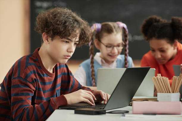 istock Side view teenage schoolboy using laptop computer in school classroom 1492537701