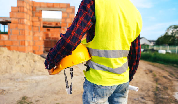 istock Construction worker on site zone. Worker in yellow vest holding hard hat and staying in front of the building zone. Construction worker on the work zone. 1492538203