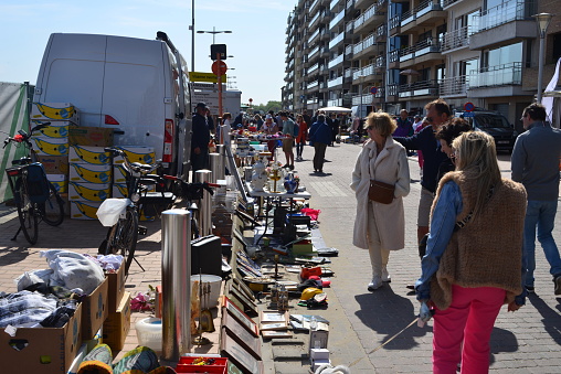 Blankenberge, West Flanders, Belgium - May 20, 2023: Vendor sells wares on the footpath, second hand objects for sale as tourists walk by